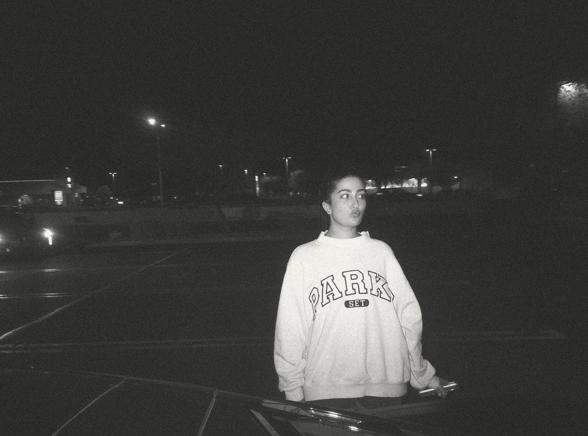 A black-and-white DigiFilm photo of a woman in a sweatshirt standing beside a car at night.
