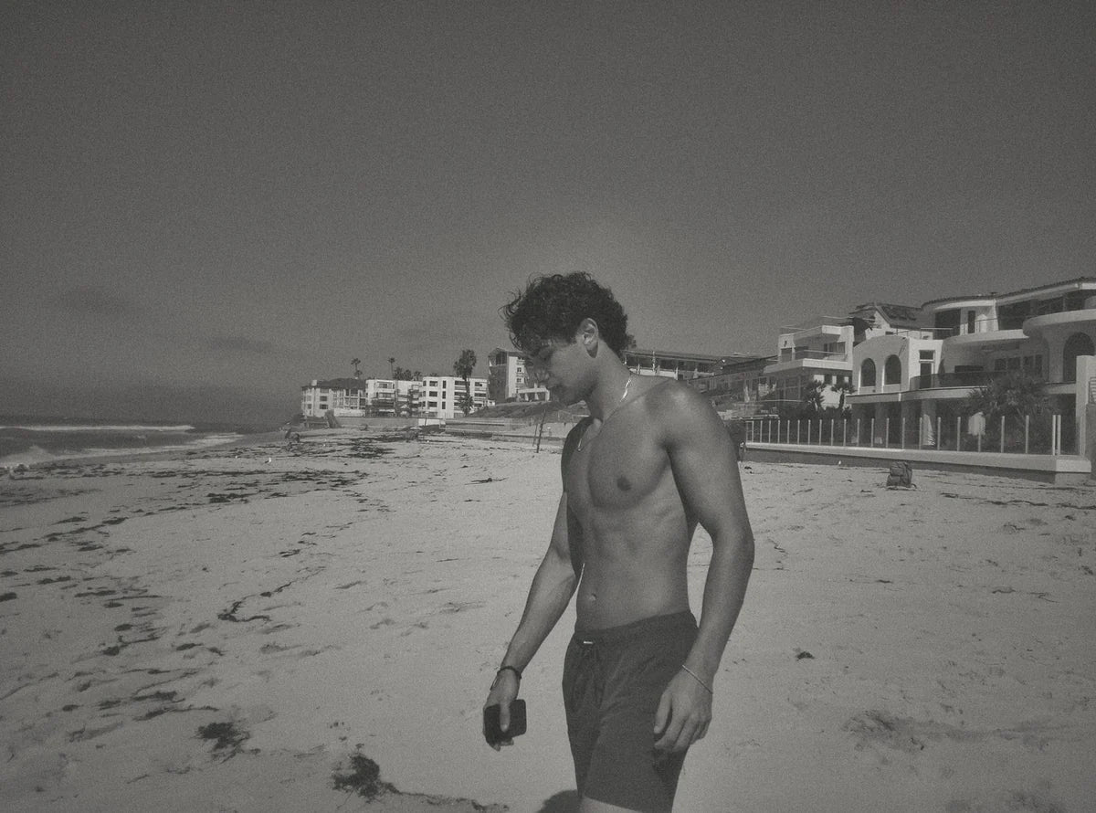 A black-and-white DigiFilm photo of a man walking along the beach beside coastal homes.