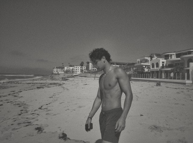 A black-and-white DigiFilm photo of a man walking along the beach beside coastal homes.